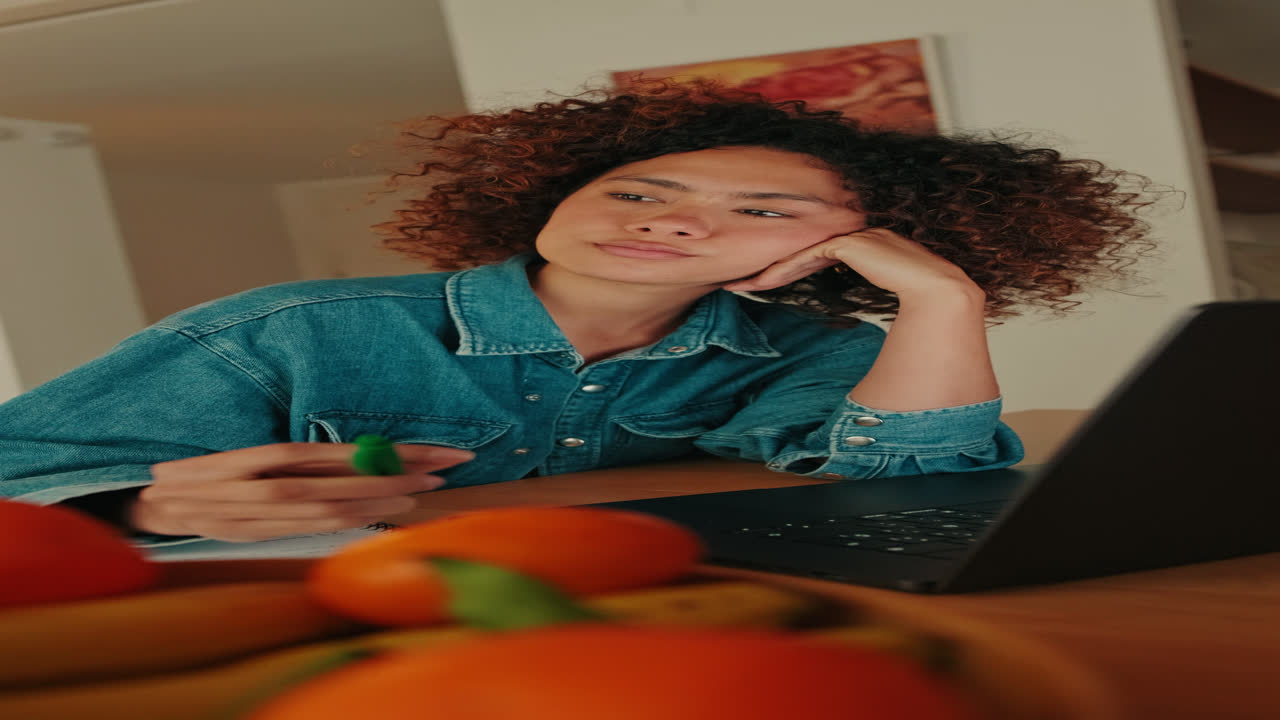 Tankefull ung kvinne jobber eller studerer på laptop hjemme