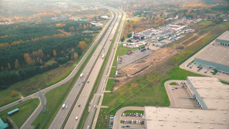 Buildings-of-logistics-center,-warehouses-near-the-highway,-view-from-height,-a-large-number-of-trucks-in-the-parking-lot-near-warehouse