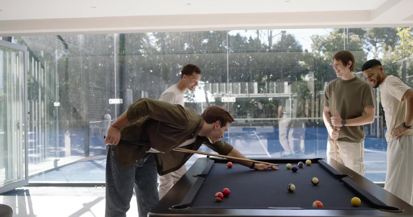 Diverse men discussing ball layout urging green-shirt man lining shot in game room on felt table