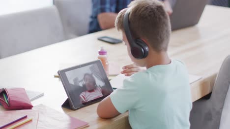 Fröhlicher-Kaukasischer-Junge,-Der-Am-Tisch-Sitzt-Und-Ein-Tablet-Für-Videoanrufe-Nutzt,-Zeitlupe