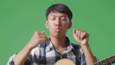 primer plano de un adolescente asiático con un baile de guitarra en el fondo de la pantalla verde