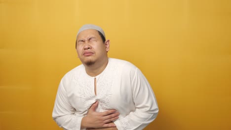 young muslim asian man squezze his stomach for having stomachache pain, against yellow background