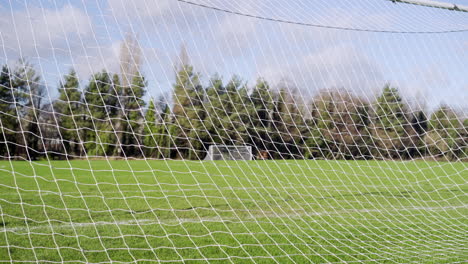 Fußballnetz,-Das-Sich-Hinter-Dem-Tor-Bewegt,-Grünes-Gras,-Blauer-Himmel-Und-Bäume