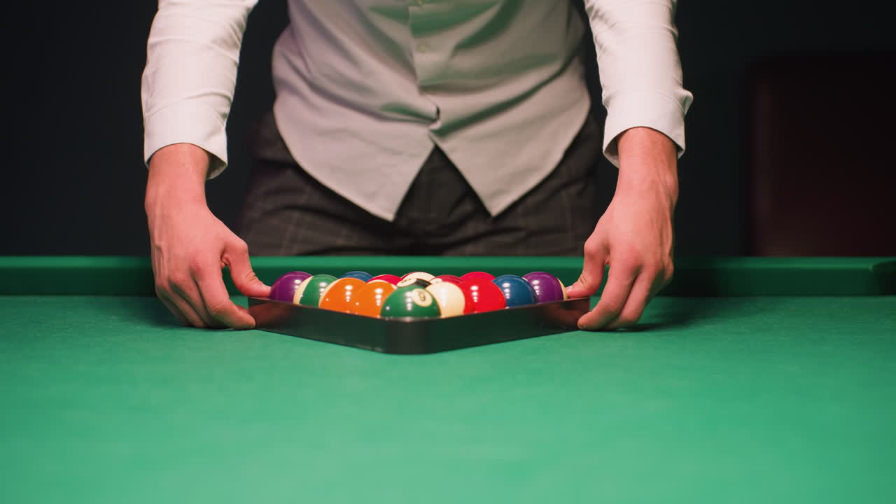 Primo piano di un giocatore di biliardo con una camicia bianco sporco, profondamente concentrato e calmo su sfondo scuro. L'illuminazione dall'alto crea una luce soffusa mentre la telecamera zooma lentamente sulle sue mani