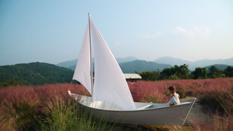 pretty girl playing in wooden sail boat pretend being sailor at pink muhly grass field - herb island farm in pocheon - eco tourism in south korea