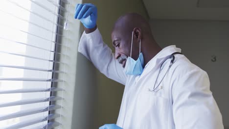 portrait of african american male doctor wearing face mask talking using smartphone