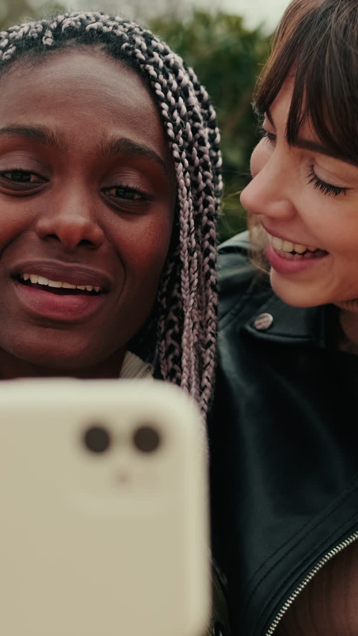 Due amici multietnici felici che sorridono e parlano allo smartphone