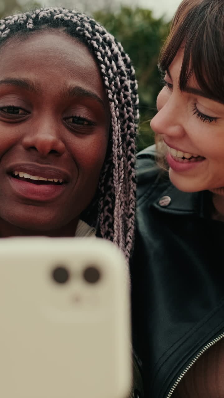 Due amici multietnici felici che sorridono e parlano allo smartphone