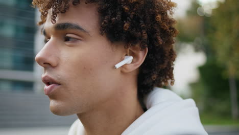 serious model face talking earphones at street portrait. curly guy using earbuds