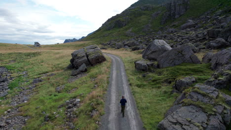 Turista-Caminando-Solo-Entre-Rocas-En-Un-Camino-De-Grava-Solitario,-Toma-Aérea-De-Reenvío