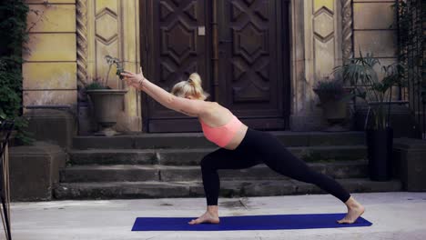 Mujer-Haciendo-Yoga-Sobre-Un-Porche-Con-Una-Gran-Puerta-De-Madera,-Vista-Frontal