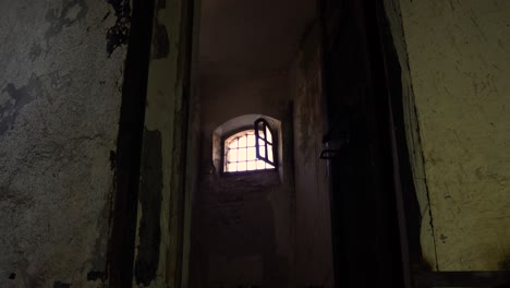 Opening-door-of-the-dungeon-with-dirty-walls-and-small-window-with-iron-bars