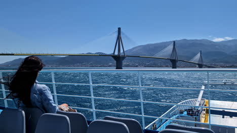 attractive woman on a ferry with a view of the rio–antirrio bridge or charilaos trikoupis bridge, greece