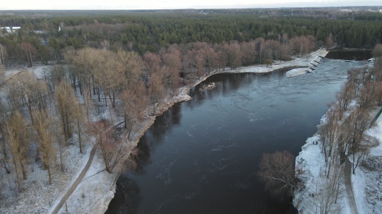 A breathtaking aerial view of Valmiera city, showcasing the winding Gauja River surrounded by snow-covered landscapes and residential areas under a wintry sky.
