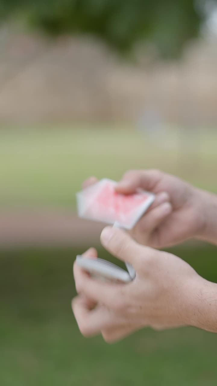 Hands performing a card manipulation trick with a deck of playing cards outdoors