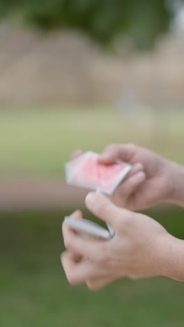 hands performing a card manipulation trick with a deck of playing cards outdoors