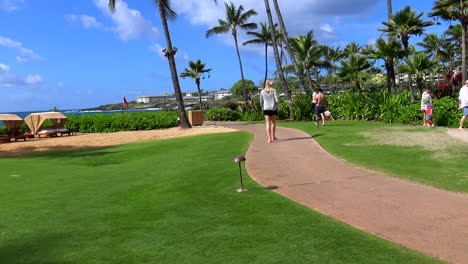 young blonde woman walks away from camera at lushly manicured resort hotel in poipu beach, garden isle, kauai, hawaii 4k