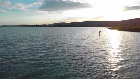 vista aérea de una mujer remando en un sup y disfrutando de unas relajantes vacaciones en una increíble puesta de sol dorada en el agua en un lago