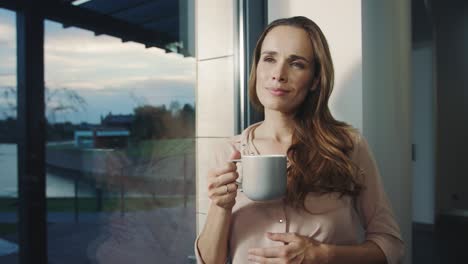 Happy-woman-staying-near-window-after-working-day.-Relaxed-woman-having-rest