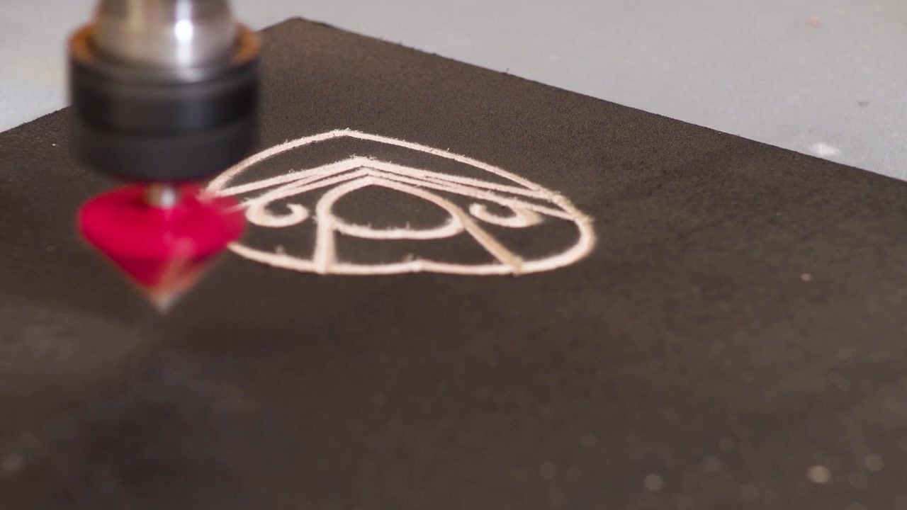 CNC-fræser graverer kalligrafi på et hjørne af MDF-træ med sort maling, 4K.