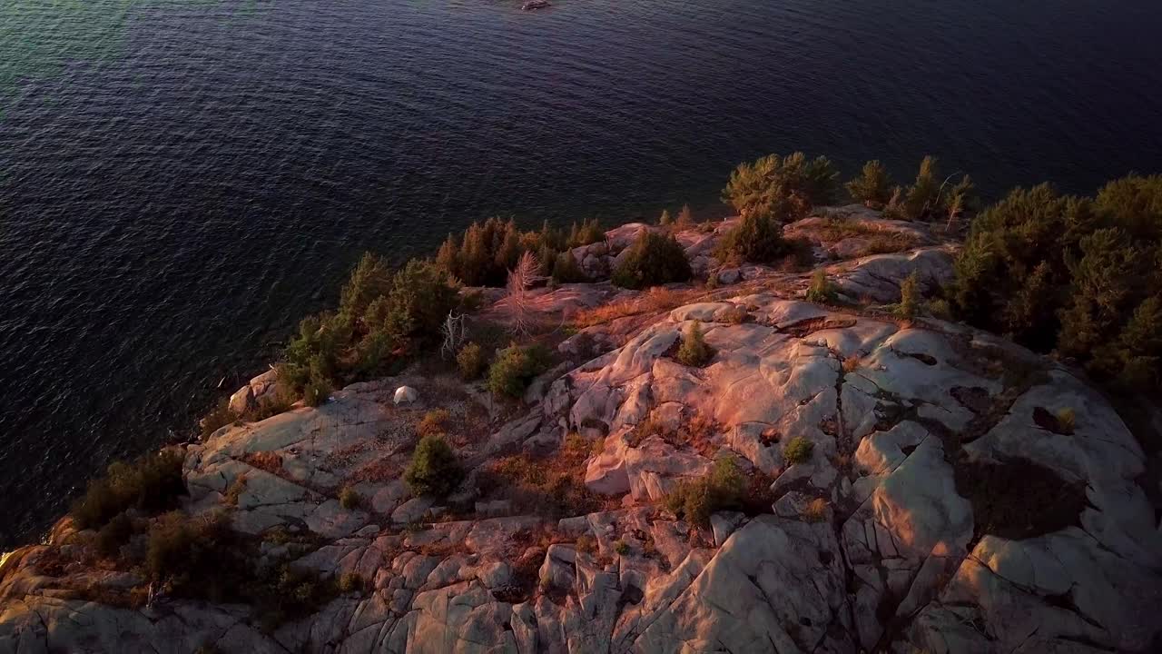 Piccola tenda bianca su un'isola rocciosa con pini in un lago blu, ripresa aerea con drone, ampia, Pedestal Down.