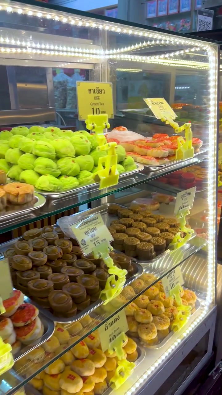 Vitrine de vidro com doces chineses variados, iluminação LED brilhante, panorâmica lenta, em um cenário de mercado movimentado.