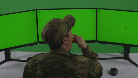 soldado trabajando en múltiples pantallas de computadora con pantallas verdes