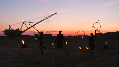 a group of professional circus performers with fire shows dance shows in slow motion using flame-throwers and rotating the torches burning objects.