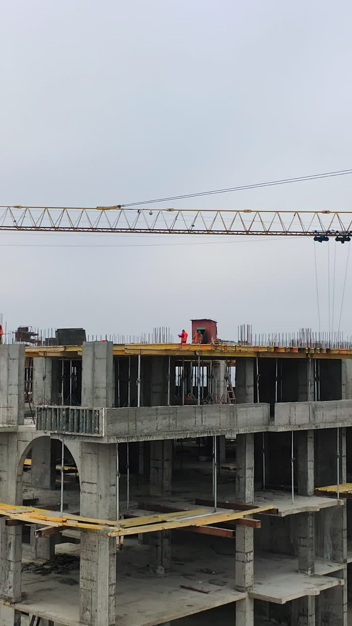 Process of construction high-rise building. Labor workers on a big construction site on the background of working crane in the city. Slow motion. Camera moves top down. Vertical video