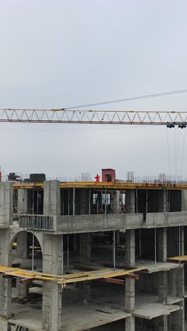 process of construction high-rise building. labor workers on a big construction site on the background of working crane in the city. slow motion. camera moves top down. vertical video