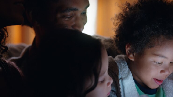 famiglia felice che usa il tablet con i bambini madre e padre che guardano i bambini giocare con la tecnologia touchscreen che si godono una serata rilassante prima di andare a letto