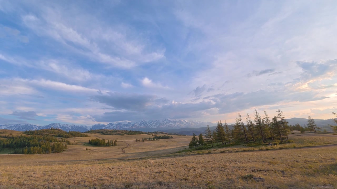 Time lapse of clouds moving over a vast alpine meadow with snow-capped Altai Mountains in the background