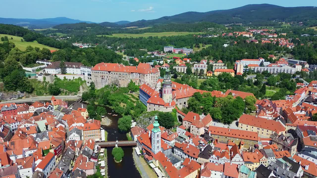 Powolne ujęcie z lotu ptaka nad zabytkowym centrum miasta. Widać wiele starych budynków i zamek pośrodku. Jest słoneczny dzień z kilkoma chmurami.