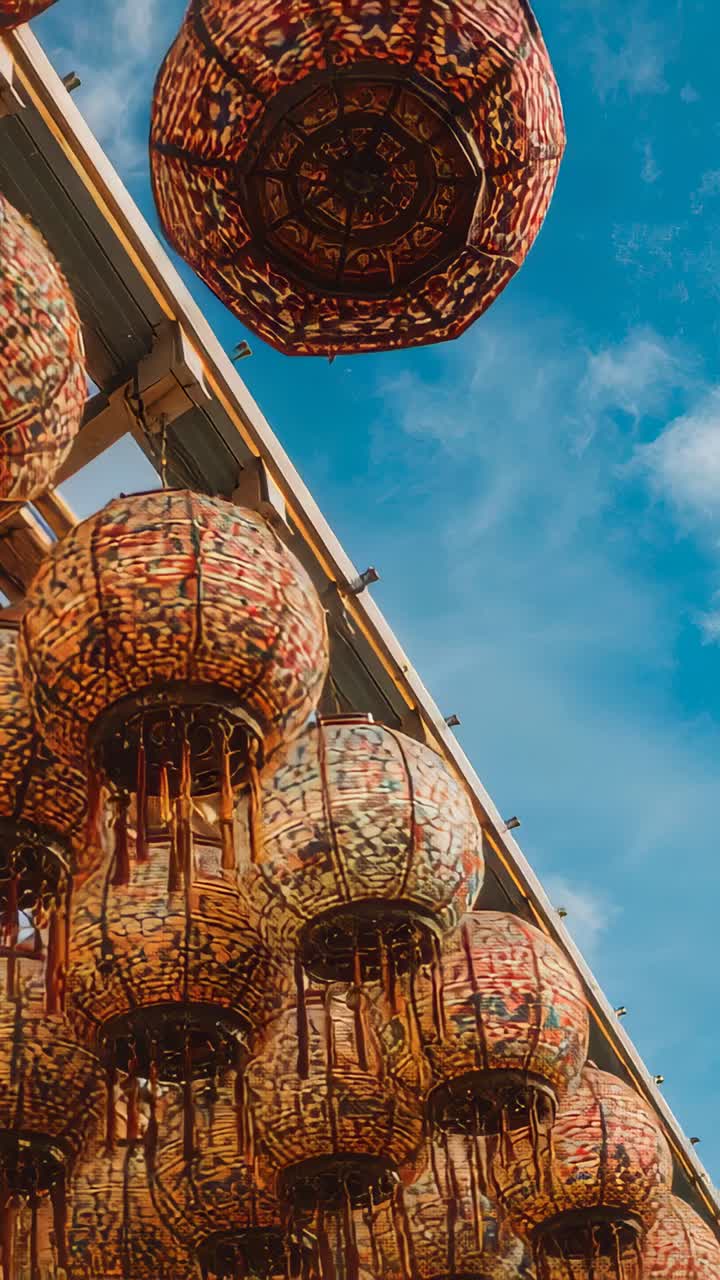 Vertical video: Tilting camera revealing ornate lanterns swaying under eave, showing beam, blue sky