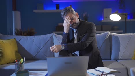 worried businessman sitting on sofa alone at home, serious and stressed businessman looking at laptop.