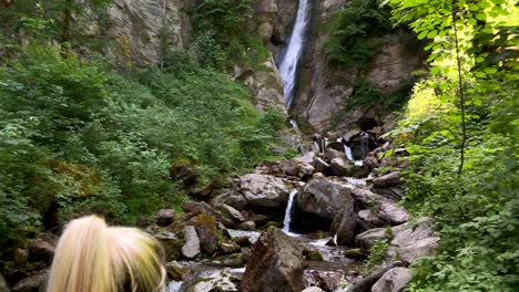 tilt up of young woman take picture of giant rural waterfall in austria during summer - 4k slow motion rear view