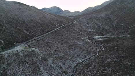 Meandering-road-through-a-snow-dusted-landscape-in-Skye-at-dusk,-serene-and-isolated,-aerial-view