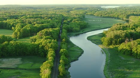 Drone-flying-back-and-up-showing-a-river-and-train-on-train-tracks-rolling-away