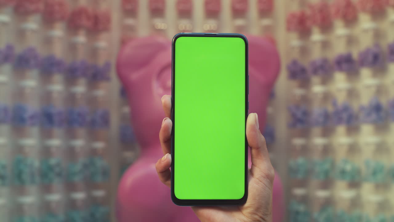 Hand holding a smartphone with a green screen against a blurred colorful background