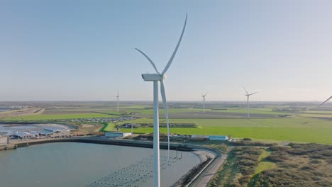 aerial slow motion shot of wind turbines and roads in a rural, coastal area in the netherlands against a blue sky on a beautiful sunny day