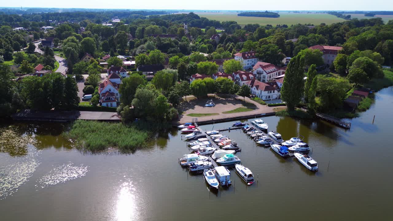 moored in a calm harbor, nestled beside a picturesque village Wustrau on the shore of a serene lake, surrounded by greenery. Nice aerial view flight panorama orbit drone