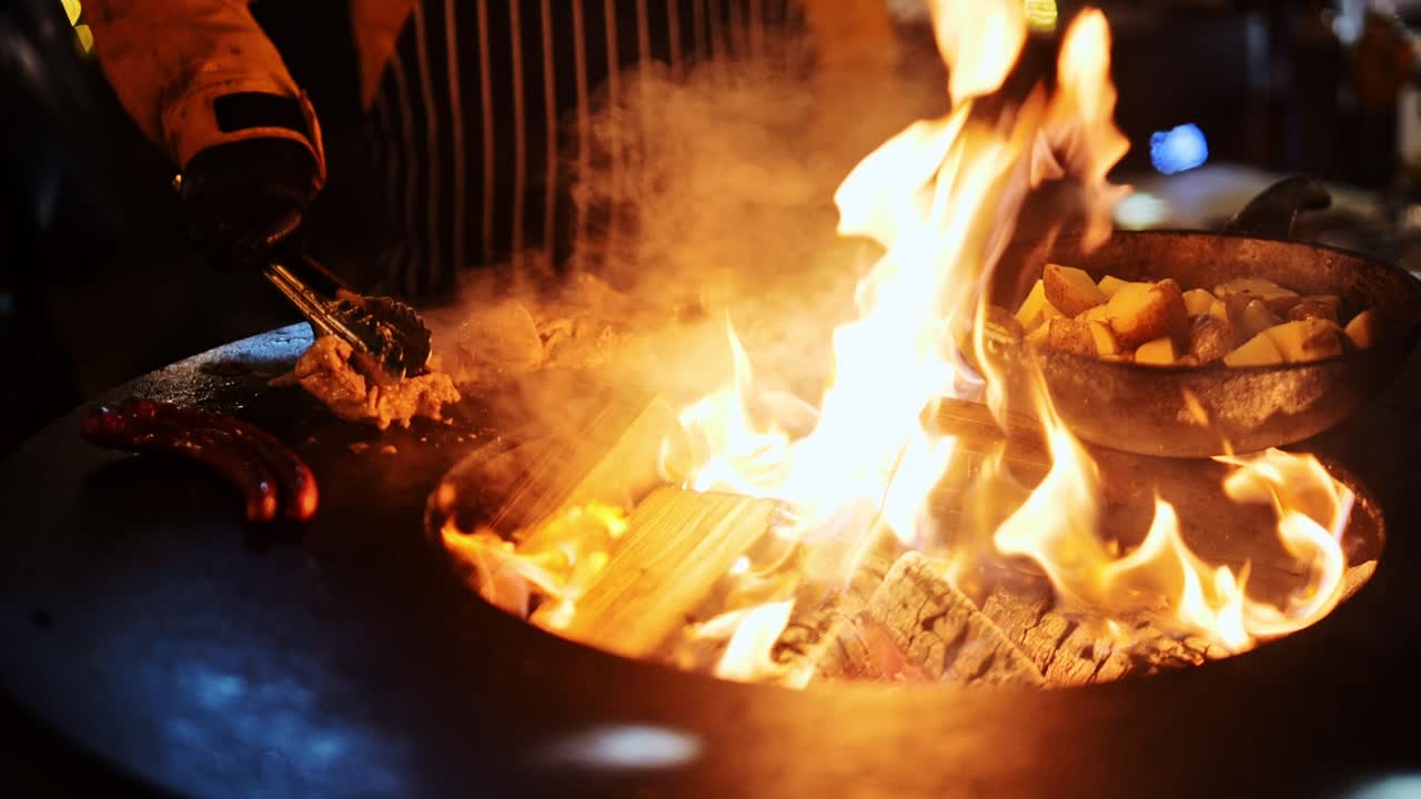 Meat and potatoes cooking over wood fire in circular grill, backyard Latvia