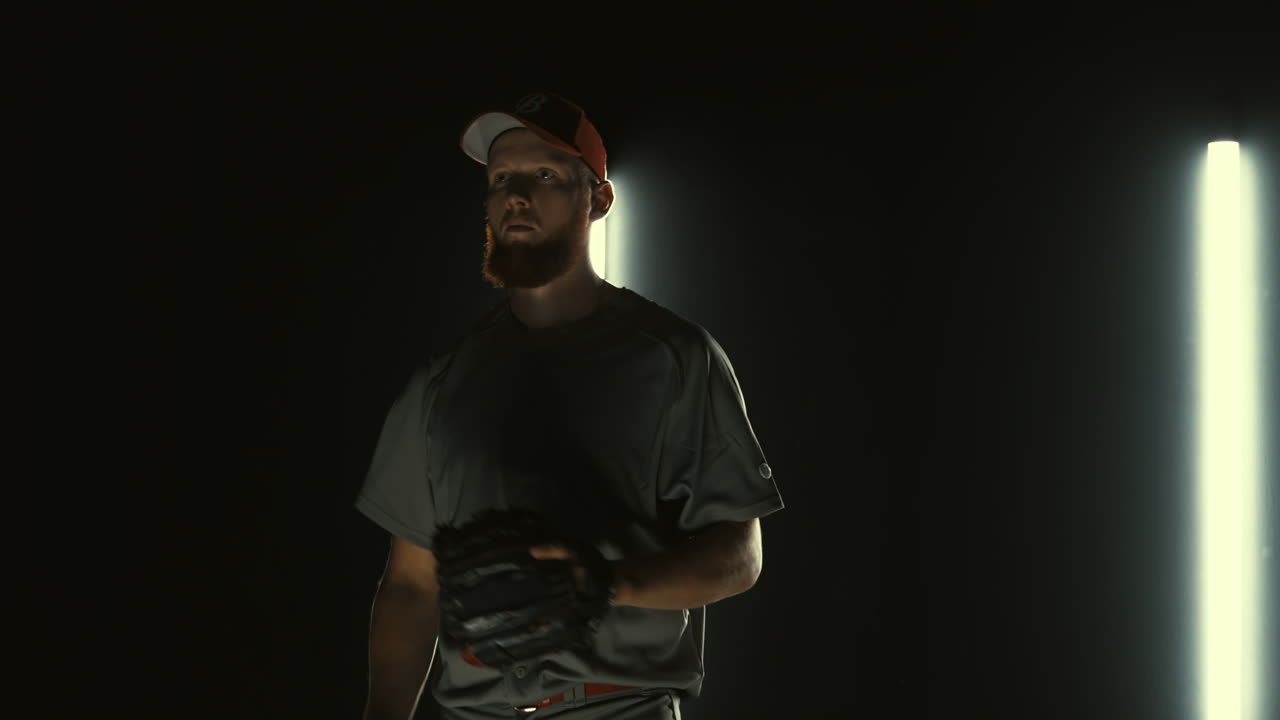 Caucasian professional baseball player pitcher throwing a ball towards camera against dark background. 4K UHD