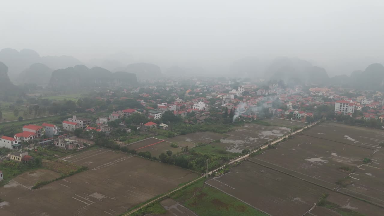 Foggy Aerial View of a Vietnamese Village Surrounded by Rice Paddies and Karst Mountains