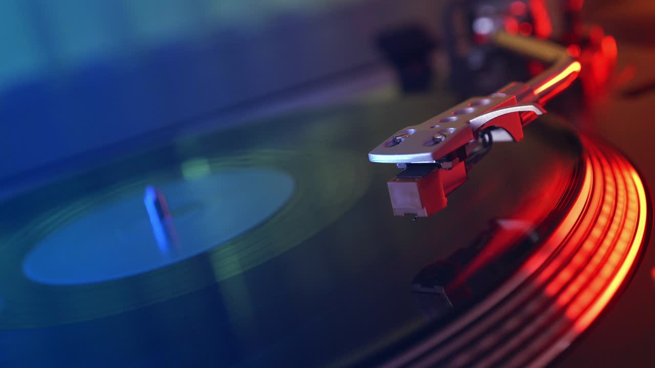 비닐 플레이어 턴테이블: 회전하는 비닐 레코드의 조각, 바늘을 클로즈업으로 가진 스타일러스, 바늘과 비닐 판을 멈추는, 매크로, 전면 뷰, 빨간색과 파란색 빛의 배경에서 흐릿한.