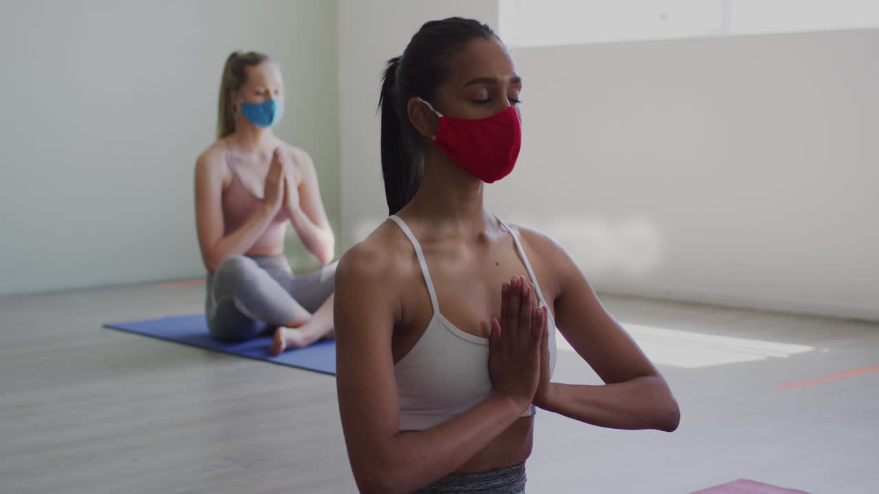 textos conceptuales de coronavirus contra dos mujeres que usan máscaras faciales practicando yoga