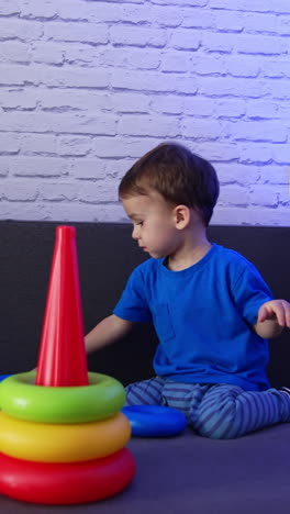 beautiful caucasian baby boy sitting on the sofa. little child playing with a toy pyramid. vertical video