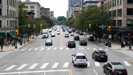 a bustling city intersection filled with numerous cars and pedestrians moving across crosswalks. tall buildings create a vibrant backdrop as traffic lights control the flow.
