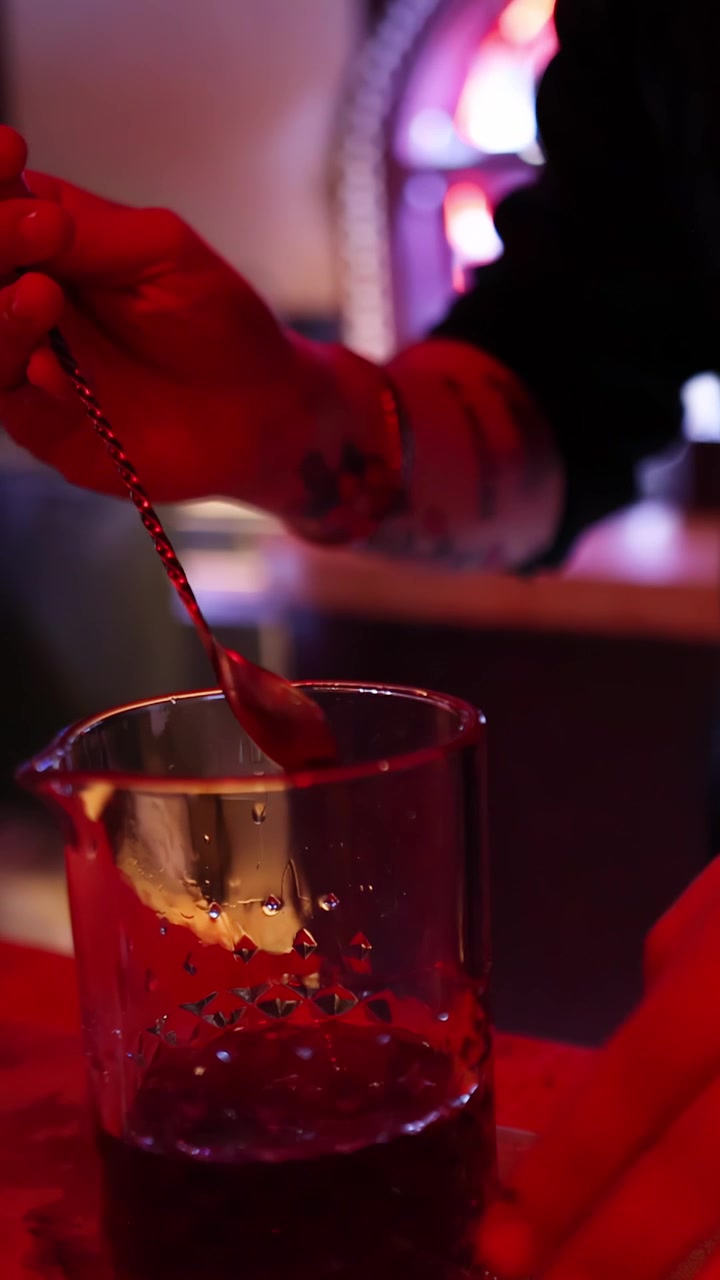 Un barman mescola un cocktail in un becher di vetro sotto un'illuminazione rossa suggestiva, prospettiva ravvicinata