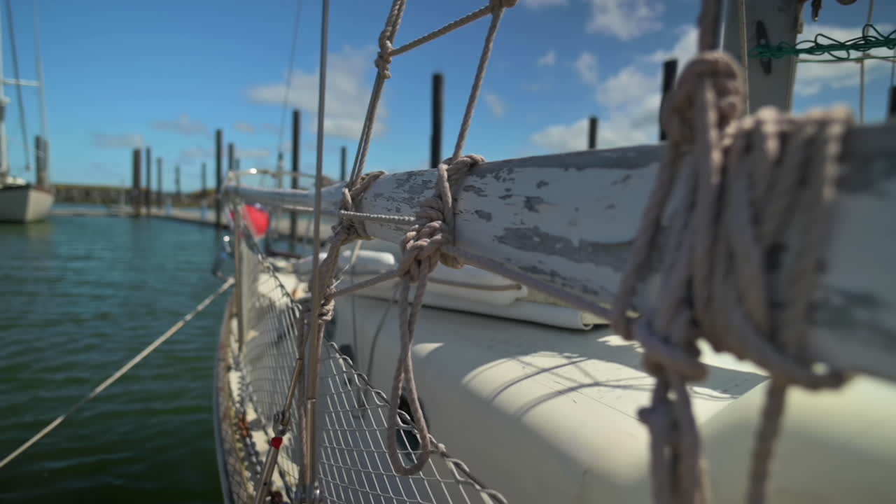 cerca de cuerdas atadas en tacos de madera de un velero con cielo brillante y aguas tranquilas en el fondo - dof superficial